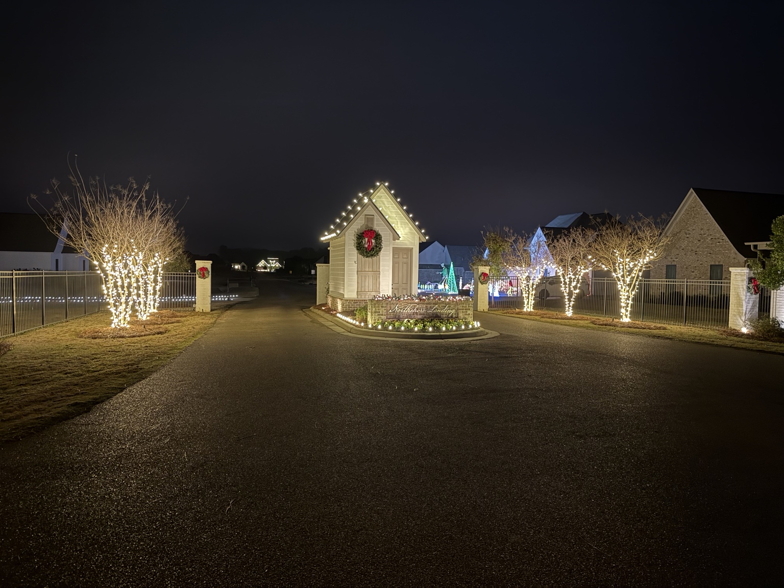 Wide view of a decorated neighborhood entrance and light-wrapped trees