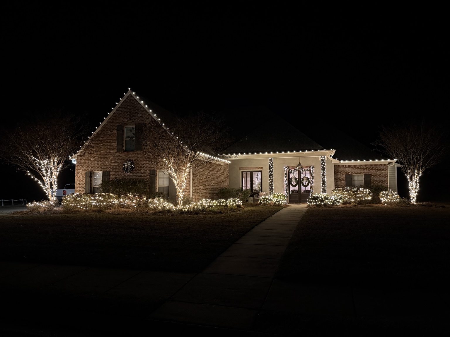 Warm white Christmas lights outlining a home, trees and shrubs